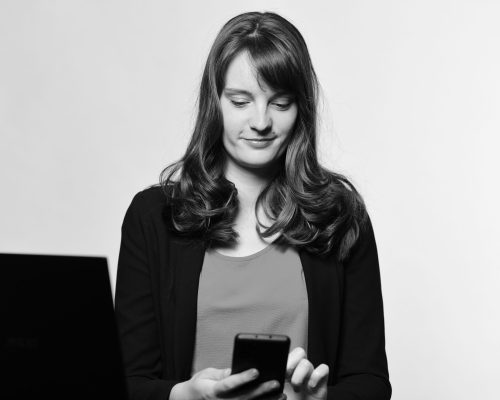 Auf dem Bild sitzt Lisa Gerth am Schreibtisch und tippt auf ihrem Smartphone